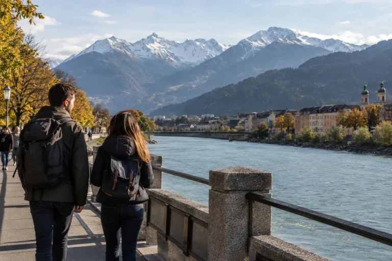 Cestovatelé na nábřeží v Innsbrucku s alpským panoramatem v dálce; ilustrační obrázek.