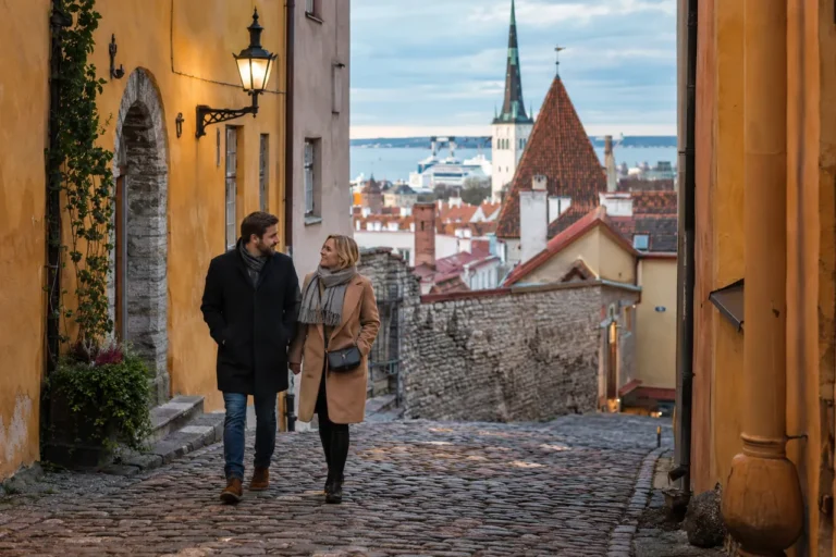 Dvojice cestovatelů prochází dlážděnou ulicí Tallinnu poblíž přístavu; ilustrační obrázek.