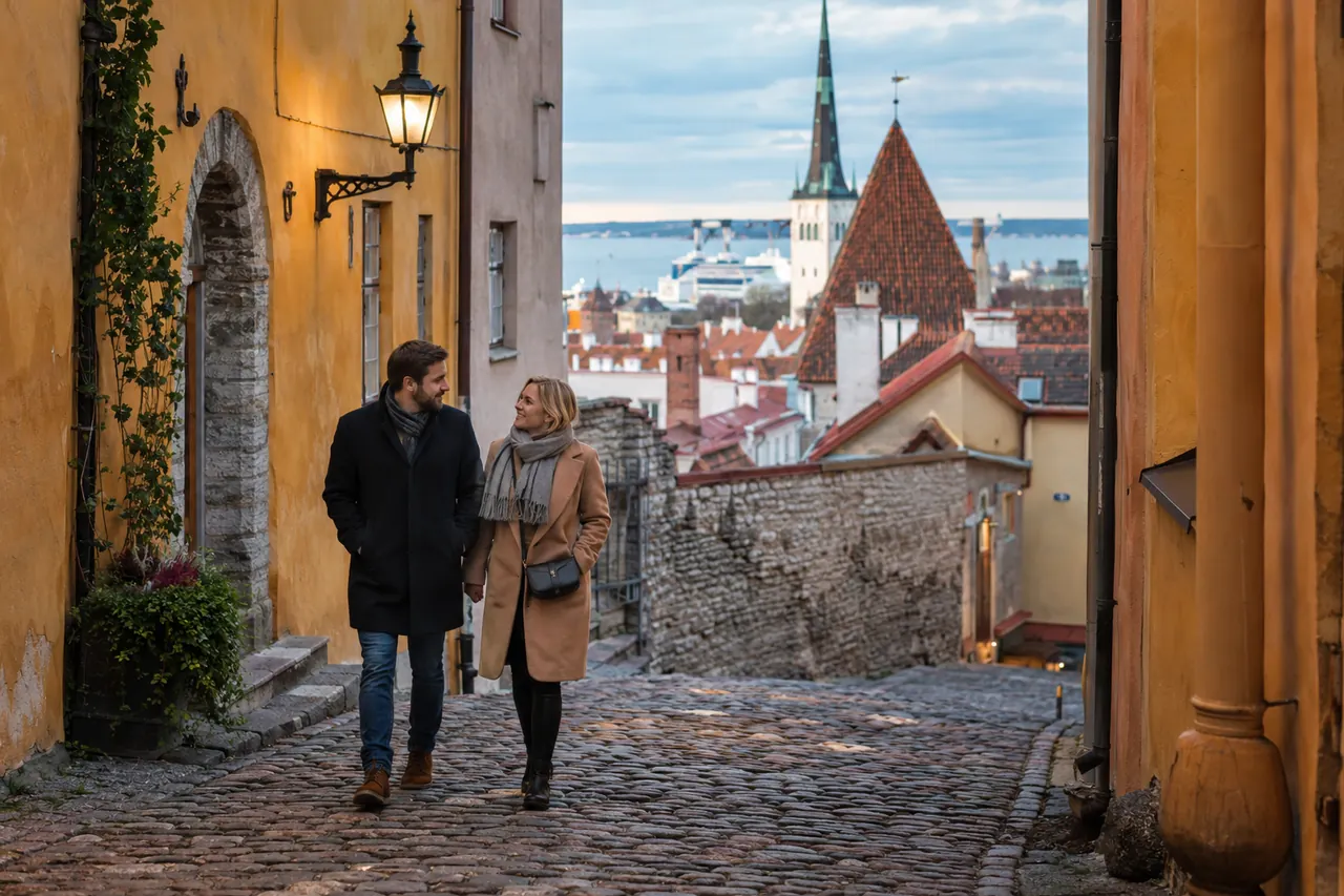 Dvojice cestovatelů prochází dlážděnou ulicí Tallinnu poblíž přístavu; ilustrační obrázek.